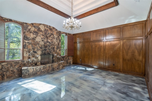 unfurnished living room with wooden walls, a stone fireplace, an inviting chandelier, and vaulted ceiling with beams