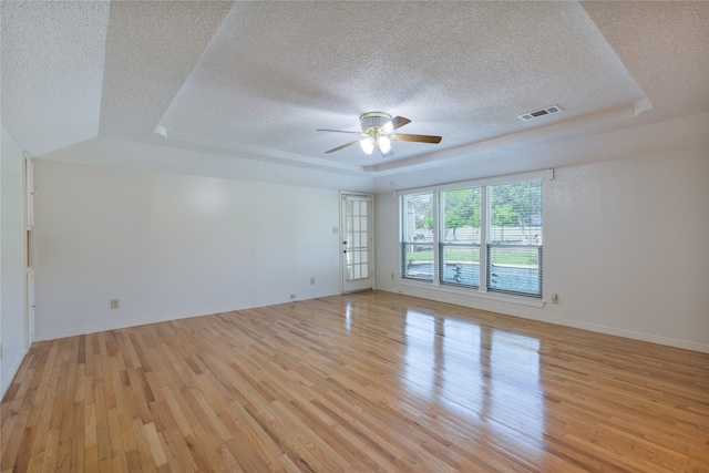 empty room featuring light hardwood / wood-style flooring, ceiling fan, a textured ceiling, and a raised ceiling