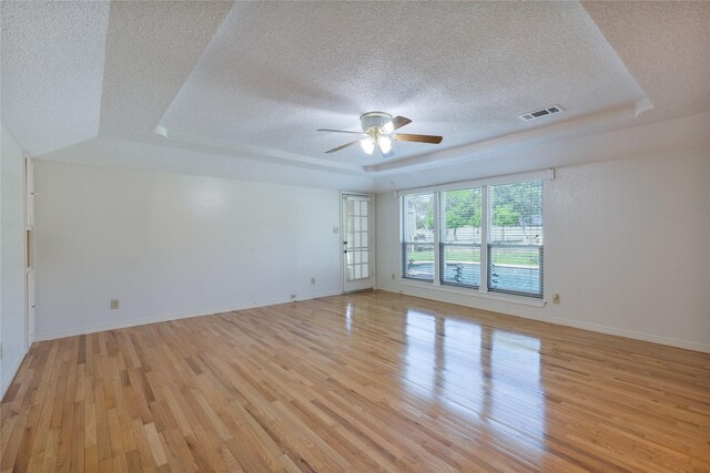 spare room with ceiling fan, a textured ceiling, light hardwood / wood-style floors, and a raised ceiling