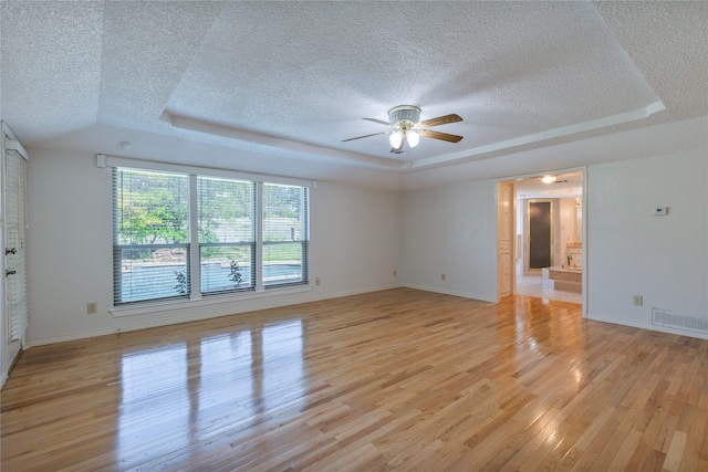 interior space with ceiling fan, a tray ceiling, a textured ceiling, and light hardwood / wood-style flooring