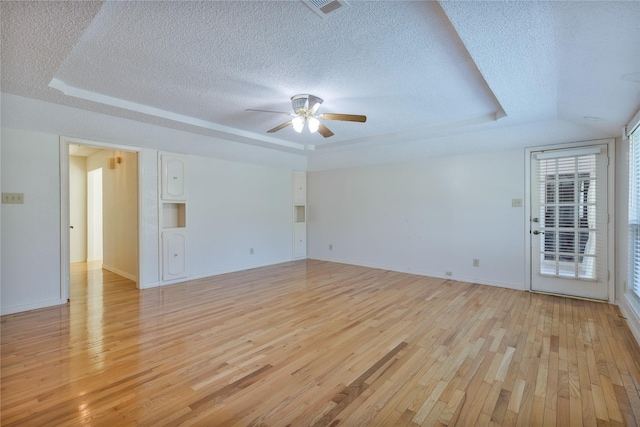 empty room featuring light wood-style floors, a tray ceiling, a textured ceiling, and a ceiling fan