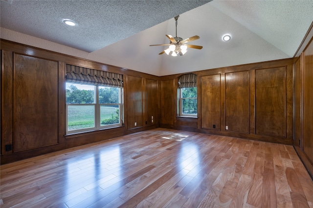 empty room with lofted ceiling, light hardwood / wood-style flooring, a textured ceiling, and ceiling fan