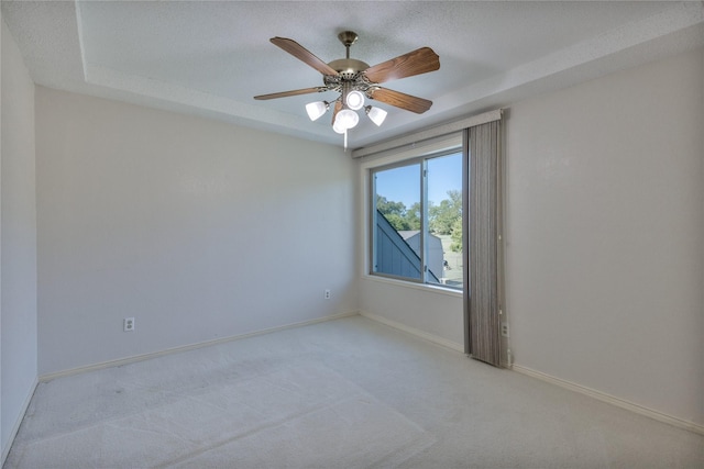 empty room featuring a raised ceiling, light colored carpet, ceiling fan, a textured ceiling, and baseboards