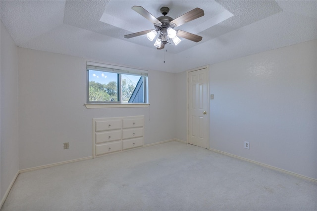 spare room featuring a textured ceiling, a tray ceiling, light carpet, and baseboards