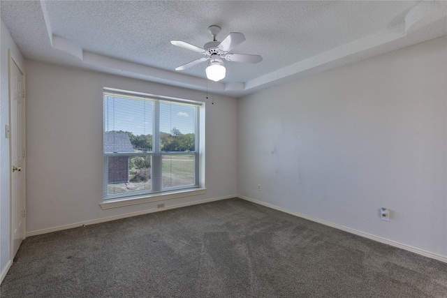 unfurnished room with a textured ceiling, ceiling fan, baseboards, dark colored carpet, and a tray ceiling