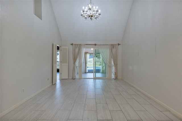 spare room with an inviting chandelier, light wood-type flooring, and high vaulted ceiling