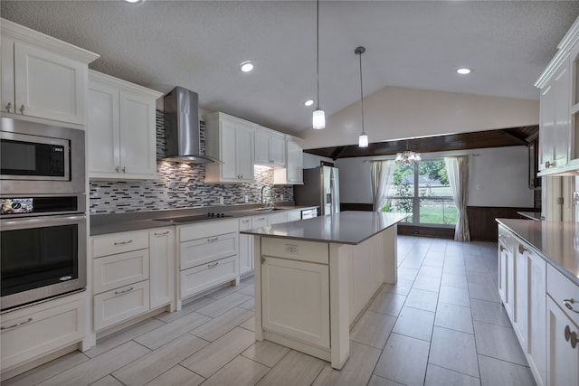 kitchen with appliances with stainless steel finishes, sink, wall chimney exhaust hood, vaulted ceiling, and white cabinets