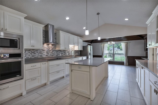 kitchen featuring a sink, white cabinets, appliances with stainless steel finishes, wall chimney range hood, and dark countertops