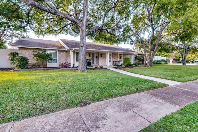 ranch-style house featuring brick siding, a front lawn, covered porch, and fence