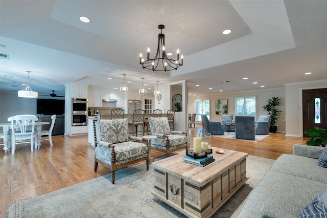 living room with light hardwood / wood-style floors, a notable chandelier, ornamental molding, and a tray ceiling