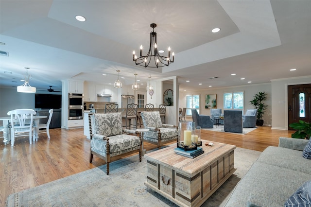 living room featuring light wood-style flooring, visible vents, recessed lighting, ceiling fan with notable chandelier, and crown molding