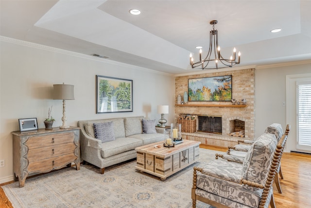 living room with an inviting chandelier, a brick fireplace, light wood-type flooring, and a raised ceiling