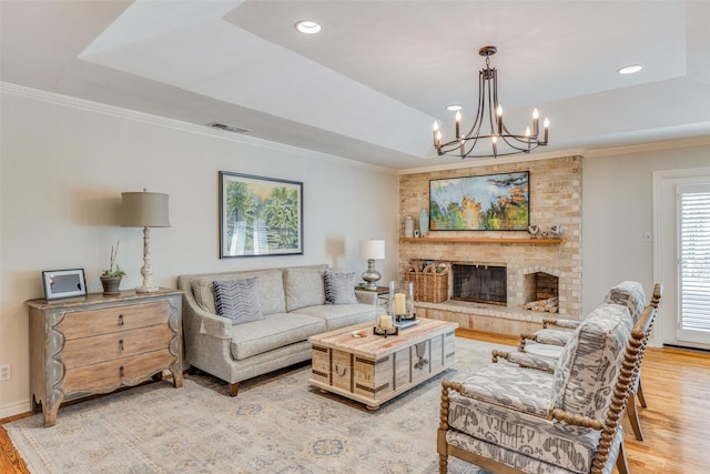 living room with crown molding, an inviting chandelier, a tray ceiling, light wood-style flooring, and visible vents