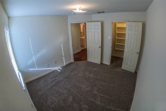 unfurnished bedroom featuring dark carpet, a closet, and a spacious closet