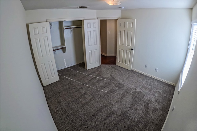 unfurnished bedroom featuring lofted ceiling, a closet, and dark colored carpet