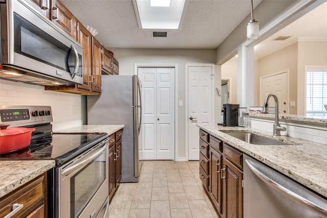 kitchen with a textured ceiling, pendant lighting, decorative backsplash, appliances with stainless steel finishes, and sink