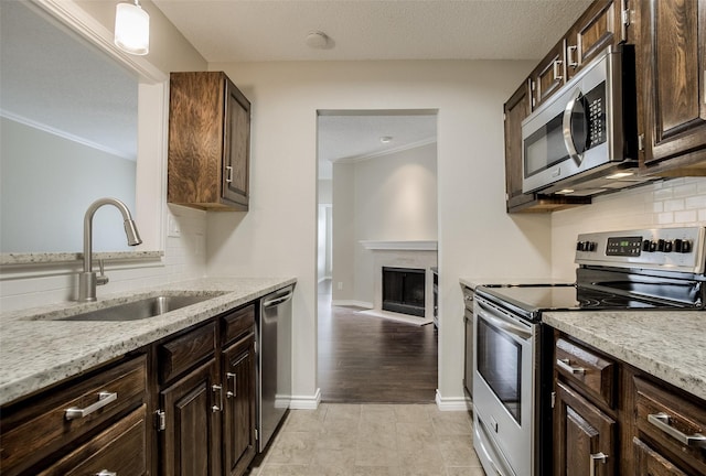 kitchen with stainless steel appliances, hanging light fixtures, light stone counters, sink, and dark brown cabinets