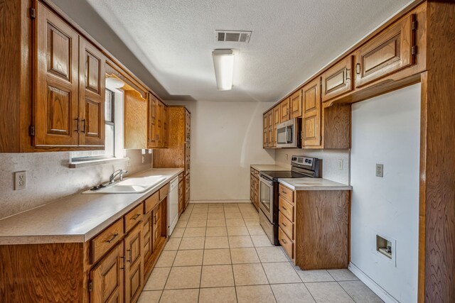 kitchen featuring stainless steel appliances, sink, light tile patterned floors, and a textured ceiling