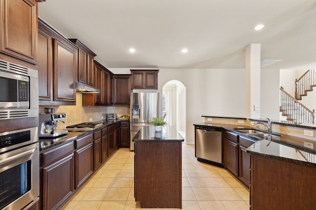 kitchen featuring light tile patterned flooring, sink, a kitchen island, appliances with stainless steel finishes, and dark stone countertops