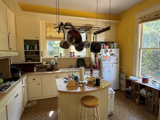 kitchen with stainless steel cooktop, sink, a kitchen island, white fridge, and pendant lighting