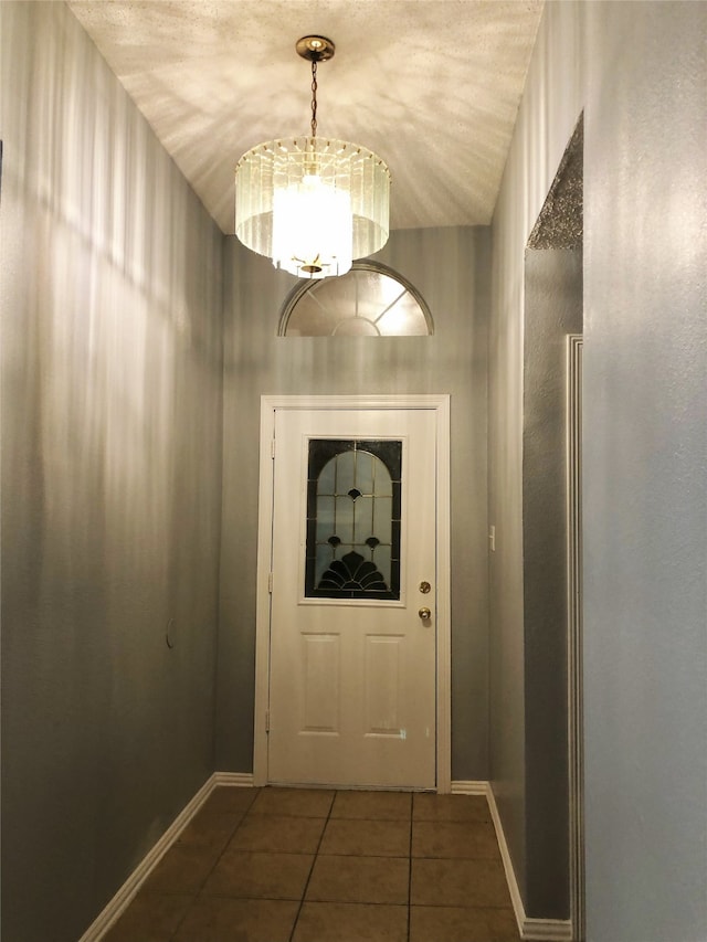 doorway with an inviting chandelier, dark tile patterned flooring, and vaulted ceiling