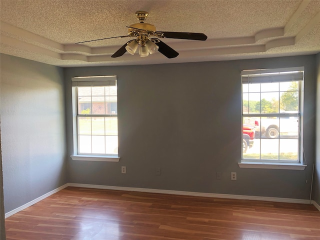 unfurnished room featuring a raised ceiling, wood-type flooring, a wealth of natural light, and ceiling fan