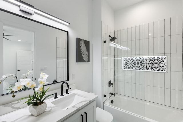 full bathroom featuring ceiling fan, vanity, tiled shower / bath combo, and toilet