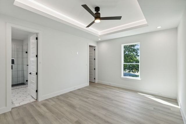 unfurnished bedroom with ceiling fan, a tray ceiling, and light hardwood / wood-style floors