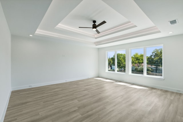 spare room featuring ceiling fan, light wood-type flooring, and a tray ceiling