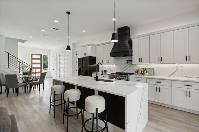 kitchen featuring an island with sink, sink, black fridge with ice dispenser, and white cabinetry