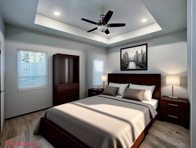 bedroom with light wood-type flooring, ceiling fan, and a raised ceiling