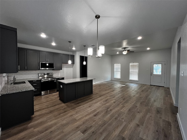 kitchen with sink, a kitchen island, decorative light fixtures, appliances with stainless steel finishes, and dark hardwood / wood-style flooring