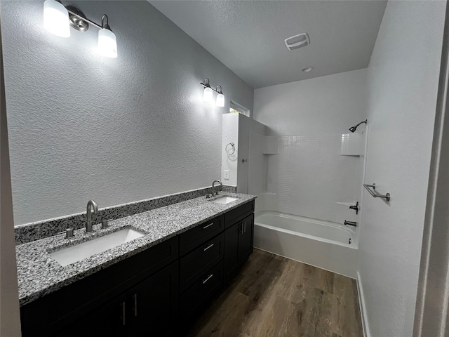 bathroom with a textured ceiling, hardwood / wood-style flooring, vanity, and  shower combination