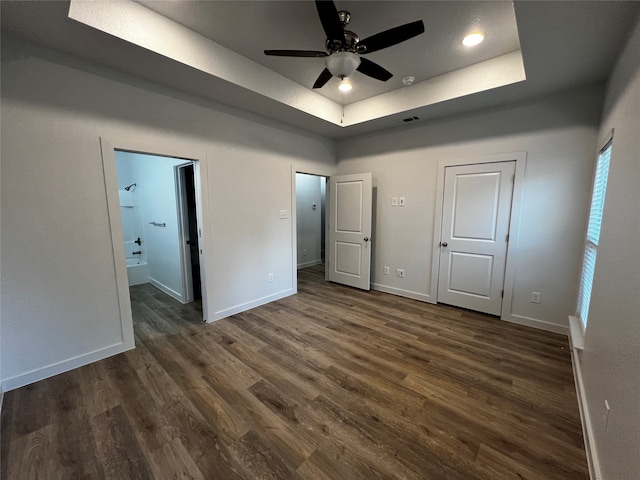 unfurnished bedroom with dark wood-type flooring, a tray ceiling, connected bathroom, and ceiling fan