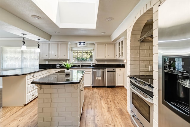 kitchen with a kitchen island, hanging light fixtures, white cabinetry, light wood-type flooring, and appliances with stainless steel finishes