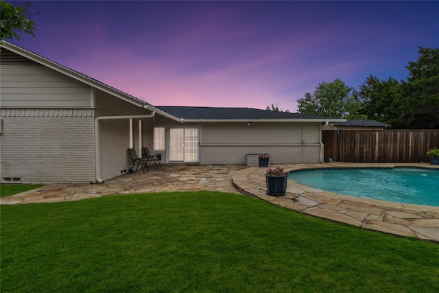 pool at dusk featuring a patio and a lawn