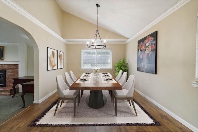 dining area with lofted ceiling, dark hardwood / wood-style floors, crown molding, a notable chandelier, and a fireplace