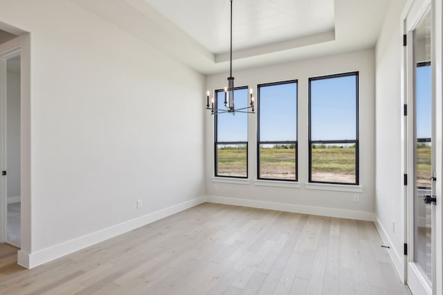 unfurnished dining area with light wood-type flooring, a tray ceiling, and an inviting chandelier