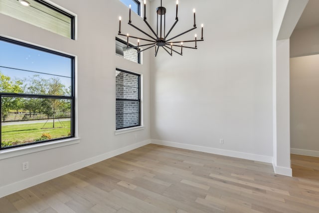 unfurnished room with a high ceiling, light hardwood / wood-style floors, plenty of natural light, and a chandelier