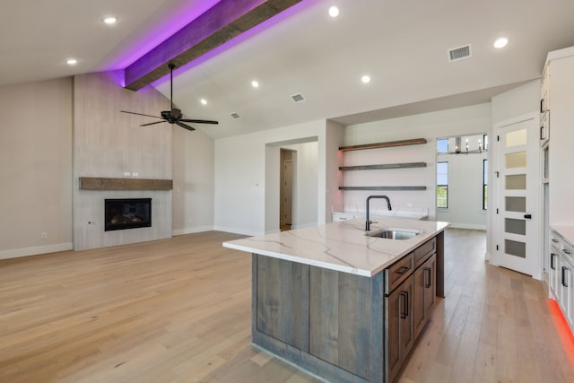 kitchen featuring sink, lofted ceiling with beams, a fireplace, light stone countertops, and light hardwood / wood-style floors