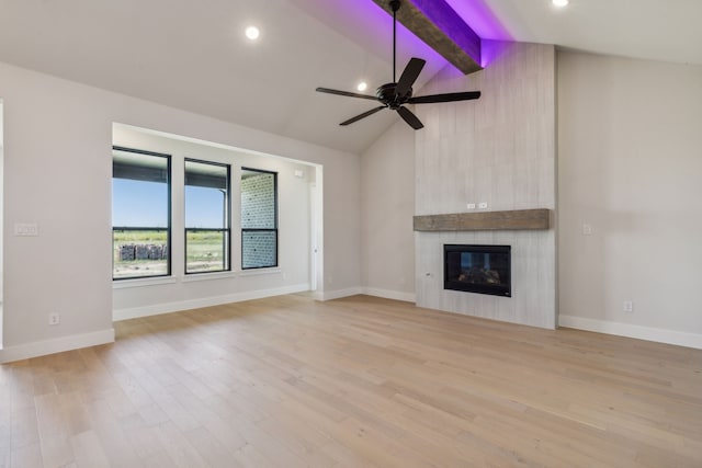 unfurnished living room with ceiling fan, beam ceiling, high vaulted ceiling, a large fireplace, and light wood-type flooring