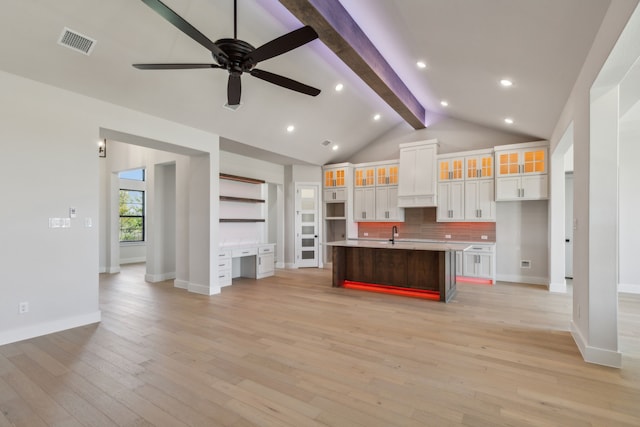 kitchen with ceiling fan, vaulted ceiling with beams, a large island with sink, white cabinetry, and light wood-type flooring