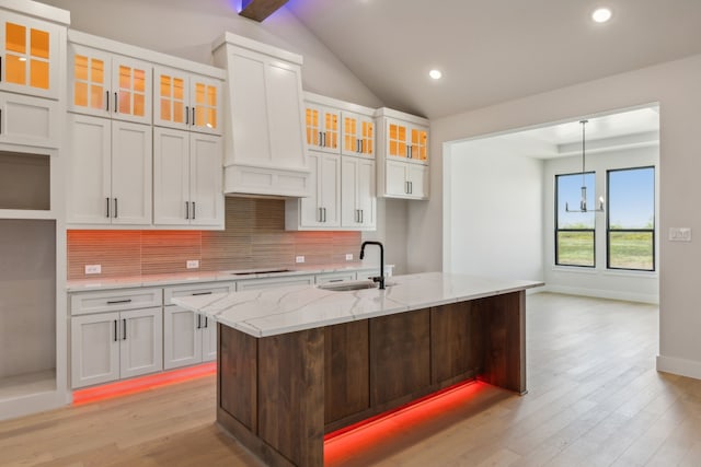 kitchen featuring an island with sink, white cabinets, sink, vaulted ceiling with beams, and backsplash