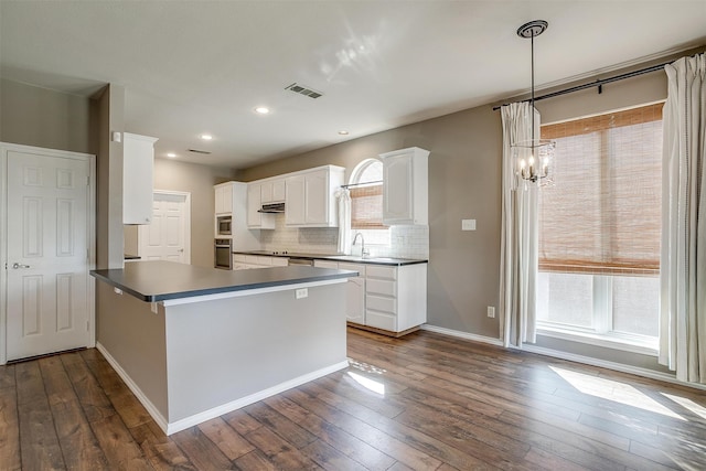 kitchen featuring kitchen peninsula, tasteful backsplash, decorative light fixtures, white cabinetry, and dark hardwood / wood-style flooring