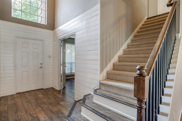 entrance foyer featuring wooden walls, dark wood-type flooring, and a towering ceiling