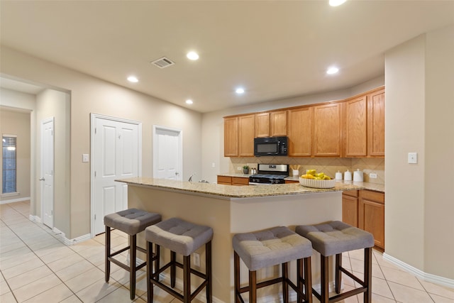 kitchen with an island with sink, a kitchen breakfast bar, stainless steel range, light tile patterned floors, and backsplash