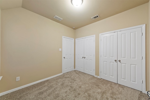 unfurnished bedroom with multiple closets, lofted ceiling, and carpet