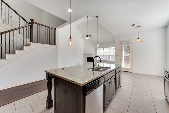 kitchen with an island with sink, light stone countertops, stainless steel dishwasher, sink, and vaulted ceiling