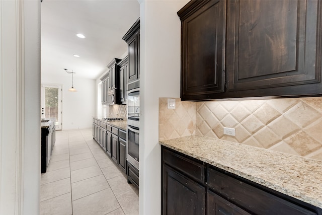 kitchen featuring light stone countertops, dark brown cabinetry, decorative backsplash, light tile patterned flooring, and hanging light fixtures