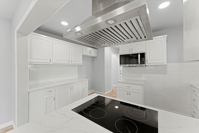 kitchen featuring stainless steel microwave, ventilation hood, light stone countertops, white cabinets, and black electric cooktop